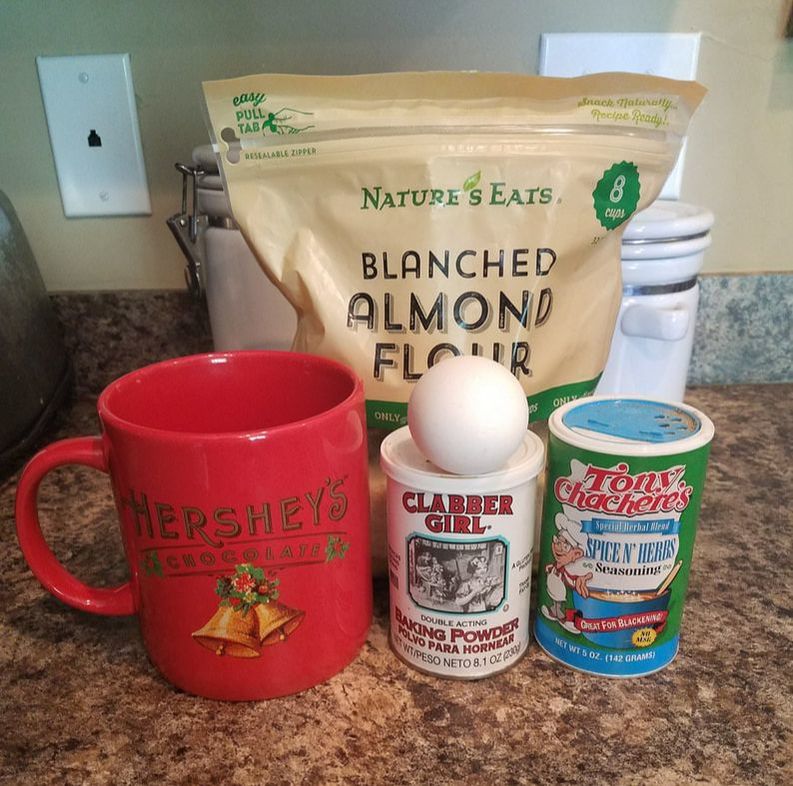 Bag of almond flour, baking powder, 1 egg, Tony Chachere's seasoning, and large coffee mug on countertop.