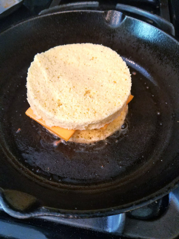 Cooked top and bottom bread with cheese in the middle being fried in butter on iron skillet.