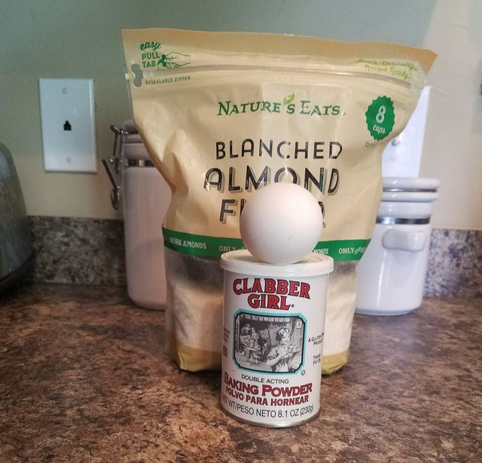 Bag of almond flour, baking powder, and an egg on a countertop.